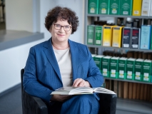 Präsidentin Sabine Riewenherm sitzt in der Bibliothek mit einem Buch in der Hand