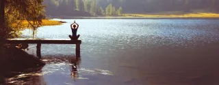 Frau macht Yoga auf einem Steg an einem See