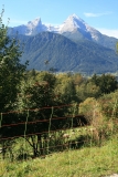 Zu sehen ist ein elektrischer Netzzaun, hinter dem eine Gruppe von Schafen vor einem Bergpanorama weidet