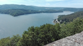 Von der exponierten Burganlage Waldeck eröffnet sich ein Weitblick auf den Edersee und den daran angrenzenden Kellerwald. Es ist ein sonniger Sommertag. Das Wasser schimmert bläulich.