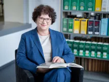 Präsidentin Sabine Riewenherm sitzt in der Bibliothek mit einem Buch in der Hand