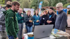 Teilnehmende stehen vor einem Tisch und schauen sich auf einem Laptop etwas an.