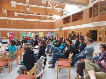 Teilnehmende des MAB Jugendforums sitzen in Stuhlreihen hintereinander in einer Mehrzweckhalle und hören einem Vortrag zu. In Hintergrund stehen Rollups.