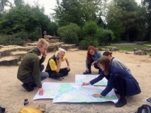 Auf der Spielfläche liegen Karten auf dem Sand und 5 Mitarbeiter machen Eintragungen.