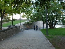 Weg mit Bäumen und Menschen, links eine Mauer, rechts ein Rasen