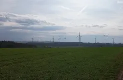 Grünland mit Waldbereichen und 66 Windenergieanlagen in unterschiedlicher Entfernung am Horizont. Hunsrück, Rheinland-Pfalz