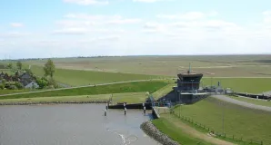 Das Foto zeigt das Sperrwerk Friedrichskoog, dass im Rugenorter Loch den Sturmflutschutz für Friedrichskoog gewährleistet. Hinter dem Hochwasserschutzteich sind die weitläufigen Salzwiesen im Wattenmeer zu sehen.
