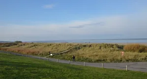 Typische Küstenlandschaft im Ostfriesischen Seemarsch in Norddeich. Hinter einem Deich ist die Weite des Wattenmeeres wahrnehmbar.