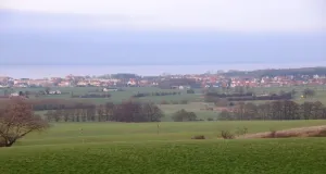 Das Foto zeigt im Vordergrund die grünlanddominierte hügelige Agrarlandschaft mit einzelnen Gehölzbeständen. Dahinter ist die Ortslage Kühlungsborn-West und die freie Ostsee zu sehen. 