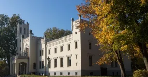 Ein weißes Schloss umgeben von alten, herbstlich gefärbten Bäumen.