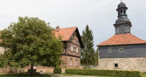 Zu sehen ist das Torhaus sowie ein Wirtschaftsgebäude der Klosteranlage Michaelstein. Eine Bank unter einem ausladenden Baum lädt zum Verweilen ein.