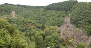 Auf zwei unterschiedlich hohen Bergspitzen ragen zwei markante Burgruinen empor. Das dunkle Gestein der Burganlagen ist sehr dominant und hebt sich deutlich von der bewaldeten Umgebung ab.