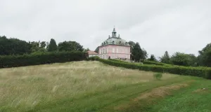 Das Foto zeigt das Fasanenschlösschen, das in der weitläufigen Parklandschaft des Schlossparks Moritzburg. Das Fasanenschlösschen ist auf einem Hügel errichtet. Zu dem Schloss führen von Hecken gesäumte Wege.