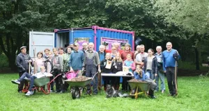 Menschengruppe mit Schubkarren vor einem Container