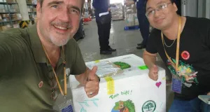 Herr Ziegler und ein Mitarbeiter des vietnamesischen Kooperationspartners sitzen vor der Box mit den Echsen und zeigen beide den Daumen hoch.