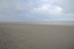 Zu sehen ist eine weite Wattlandschaft bei Wangerooge an einem bewölkten Tag.