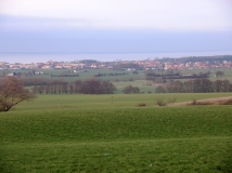 Das Foto zeigt im Vordergrund die grünlanddominierte hügelige Agrarlandschaft mit einzelnen Gehölzbeständen. Dahinter ist die Ortslage Kühlungsborn-West und die freie Ostsee zu sehen. 