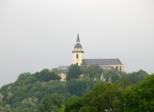 Das Foto zeigt das Kloster Siegburg auf der Spitze einer bewaldeten Anhöhe an einem regnerischen Tag.