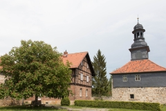 Zu sehen ist das Torhaus sowie ein Wirtschaftsgebäude der Klosteranlage Michaelstein. Eine Bank unter einem ausladenden Baum lädt zum Verweilen ein.
