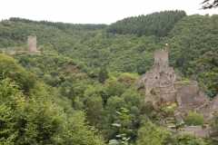 Auf zwei unterschiedlich hohen Bergspitzen ragen zwei markante Burgruinen empor. Das dunkle Gestein der Burganlagen ist sehr dominant und hebt sich deutlich von der bewaldeten Umgebung ab.