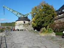 Das Foto zeigt den „Alten Kranen“ an der Uferpromenade des Mains in Würzburg. Im Hintergrund sind Weinberge zu sehen.