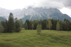 Zu sehen ist eine Wiese mit einer kleinhügeligen, buckartigen Oberfläche. Am Horizont ziehen Wolken auf und verdecken die Bergspitze des angrenzenden Karwendelgebirges.