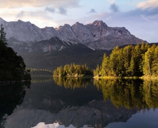 See mit Wald und Bergen im Hintergrund, im Wasser spiegelt sich die Landschaft