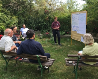 People sit outside, one person presents content on a whiteboard