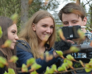 Drei Jugendliche machen im Wald Filmaufnahmen.