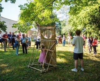 Menschengruppe auf einer Wiese, in der Mitte eine Holzkonstruktion