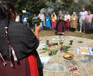 Teilnehmende des Forums in Oaxaca, die im Kreis für ein Ritual um Ernteprodukte und Blumen stehen