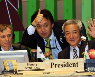 Drei Männer mit Headset sitzen bei der Vertragsstaatenkonferenz an einem Tisch