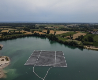 Die Luftaufnahme zeigt eine schwimmende PV-Anlage auf einem Baggersee in der Nähe von Karlsruhe. Im Hintergrund sind Felder und Häuser zu sehen.