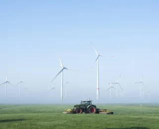 Traktor auf einer landwirtschaftlichen Fläche, im Hintergrund Windenergieanlagen