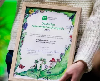 Preisträger*innen des Deutschen Jugend-Naturschutzpreises präsentieren ihre Urkunde, gestaltet von Cornelia Funke