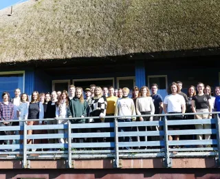 Foto der Teilnehmenden auf einem Balkon vor einem Reetdach-Haus