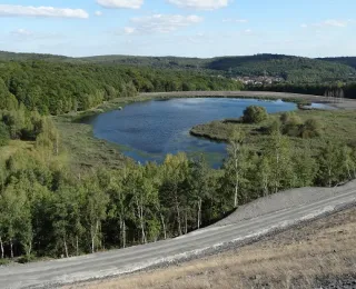 Das Foto als Schrägluftbild zeigt einen Teil einer überwiegend unbewachsenen Haldenflanke des Steinkohlenbergbaues und einen Absinkweiher der von einem geschlossenen Laubwald umgeben ist.