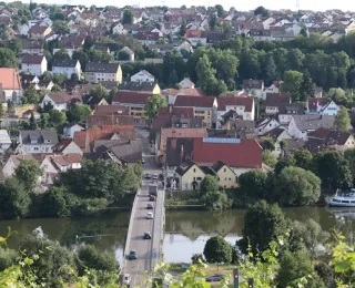 Blick auf die Gemeinde Benningen mit Neckar, Brücke über den Fluss, Wohnhäusern und Kirche mit Turm im Hintergrund.