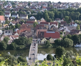 Blick auf die Gemeinde Benningen mit Neckar, Brücke über den Fluss, Wohnhäusern und Kirche mit Turm im Hintergrund.