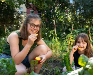 Junge Frau und junges Mädchen im Gemüsebeet verspeisen Obst