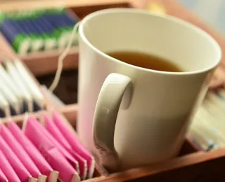 Teetasse, die in einer Teebeutelbox steht und in der ein Teebeutel im Tee hängt.