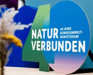 Großes, farbiges Dekorationselement mit der Zahl 40 und dem Text 'NATUR VERBUNDEN 40 JAHRE BUNDESUMWELT-MINISTERIUM' vor blauem Hintergrund