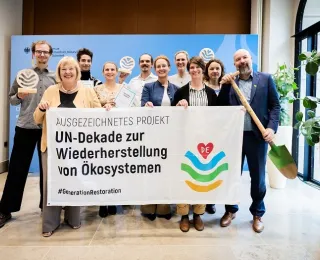 Die Gewinner*innen der UN-Dekade halten im Bundesumweltministerium ein Banner in die Kamera.