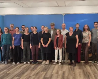 Gruppe von Menschen steht in einem Raum vor einer blauen Wand mit Landschaftsbild und Logo des Freistaats Thüringen