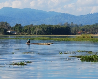 Large, calm lake with a fisherman in a small fishing boat against a background of mountains